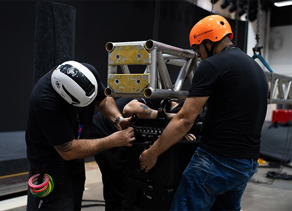 Profissionais instalando caixas acústicas em um evento.